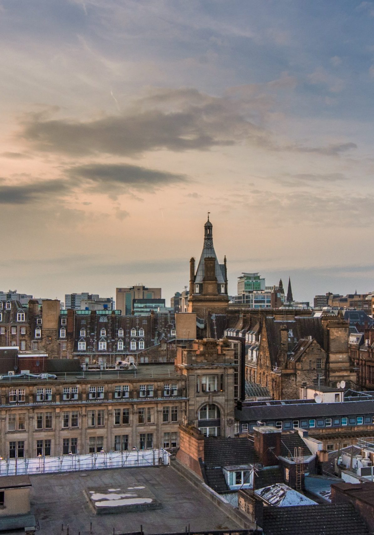 A wide rooftop view looking out over the buildings and architecture of Glasgow city centre at sunset, Scotland